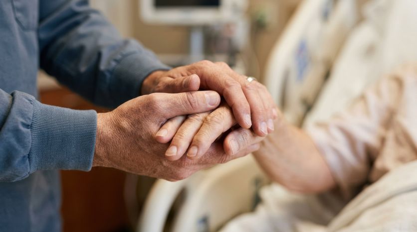 Gentle hands holding in a hospital bed, offering comfort and support to a patient La visite potentielle de Léon XIV à la Maison Jeanne-Garnier