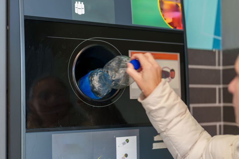 Person recycling a plastic bottle at a modern recycling station inside a city environment Initiative pour une consigne plastique remise en question